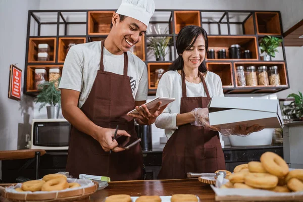 Chefs masculinos e femininos sorriem enquanto tomam notas, preparam ordens de donuts — Fotografia de Stock