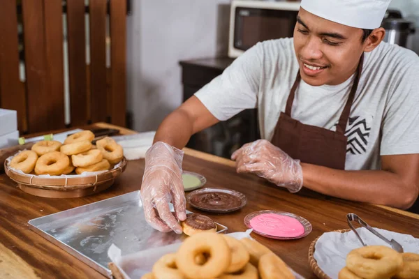 Мужчина-повар дает шоколад, чтобы украсить пончики на кухне — стоковое фото