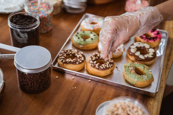 Руки в пластиковых перчатках украшают пончики — стоковое фото