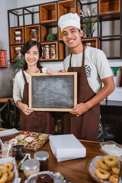 Ásia casal vestindo avental segurando um blackboard no o cozinha espaço — Fotografia de Stock