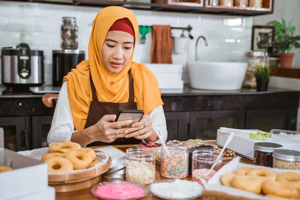 Una cuoca velata sorride con un grembiule mentre usa un cellulare — Foto Stock