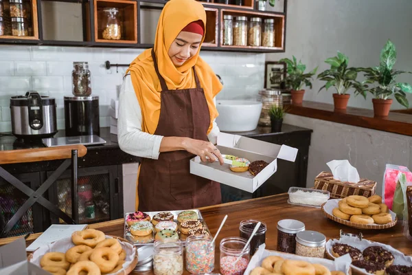 Beautiful woman in scarf preparing donuts packing into donut boxes — Stock Photo, Image