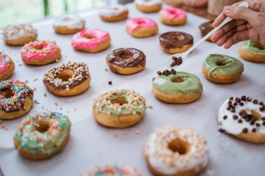 Şeflerin el kapaklarını kapatın çeşitli donutları çikolatalı şekerle süsleyin.