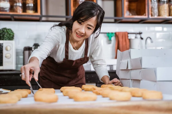 Красивые женщины в фартуках во время приготовления пончиков с щипцами пищи для украшения — стоковое фото