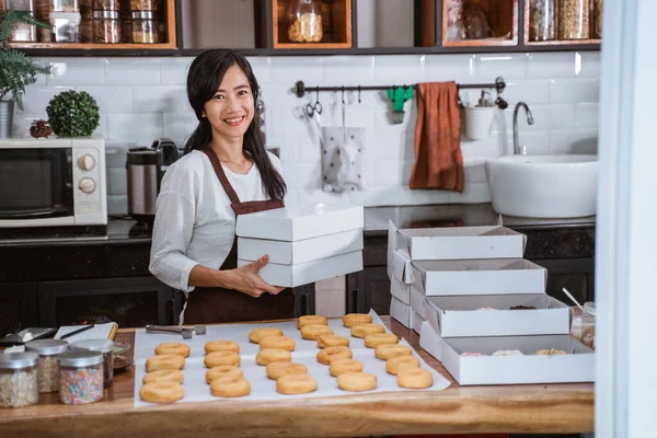 Молодая женщина с коробкой пончиков перед пончиками на столе — стоковое фото