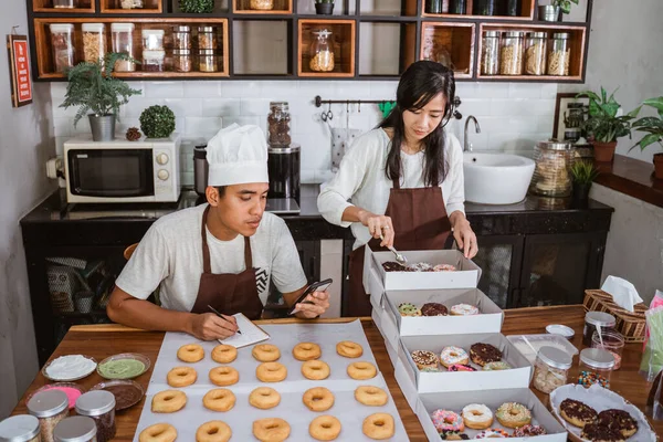 Asiático jovem casal sentado quando se prepara de donuts ordem — Fotografia de Stock