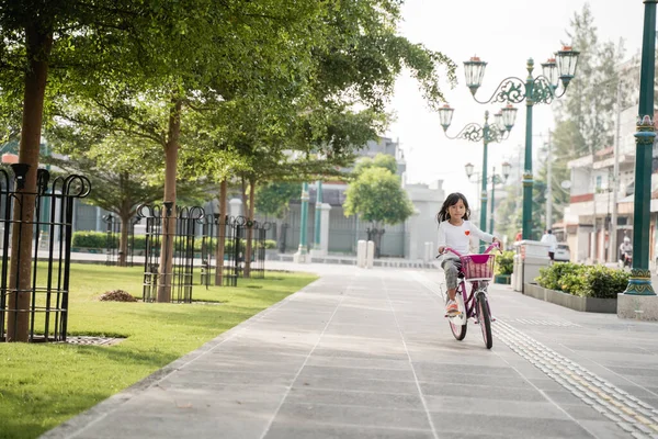 Un retrato de una niña alegre y feliz jugando una bicicleta en el parque —  Fotos de Stock