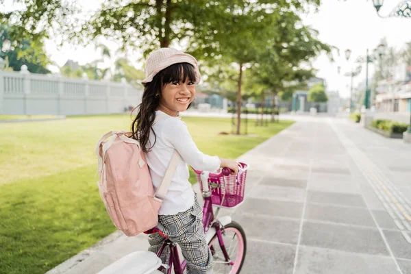 Chica montando una bicicleta en el parque yendo a la escuela por sí misma —  Fotos de Stock