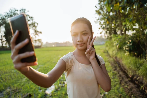 Retrato de uma bela jovem olhando enquanto segurando um celular tirar uma selfie — Fotografia de Stock