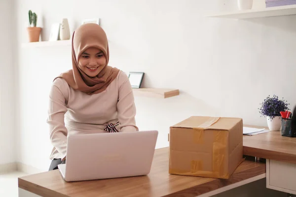 Attraktive fröhliche junge muslimische Geschäftsfrau arbeitet am Laptop und lächelt, während sie an ihrem Schreibtisch sitzt modernes Büro — Stockfoto