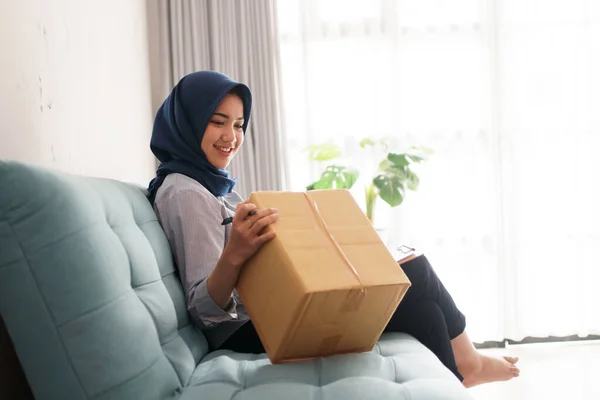 La jeune femme d'affaires musulmane attrayante et joyeuse travaille sur le paquet et sourit tout en étant assise à son bureau moderne — Photo
