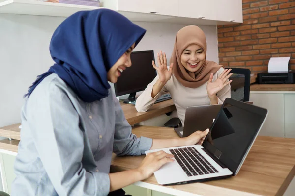 Aantrekkelijke vrolijke jonge moslim zakenvrouw werken op laptop en glimlachen terwijl zitten aan haar bureau modern kantoor met haar vriend — Stockfoto