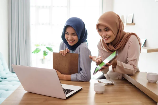 Aantrekkelijke vrolijke jonge moslim zakenvrouw werken op laptop tablet en glimlachen terwijl zitten aan haar bureau modern kantoor met haar vriend — Stockfoto