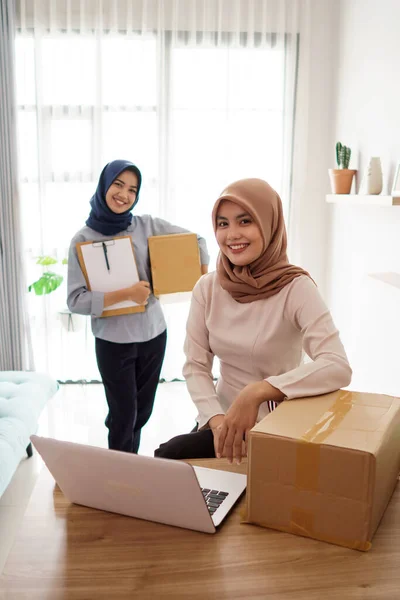 Attrayant joyeux jeune femme d'affaires musulmane travaillant sur ordinateur portable et souriant tout en étant assis à son bureau moderne avec son ami — Photo