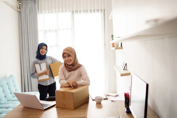 Attrayant joyeux jeune femme d'affaires musulmane travaillant sur ordinateur portable et souriant tout en étant assis à son bureau moderne avec son ami — Photo