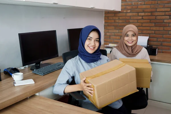 Attrayant joyeux jeune femme d'affaires musulmane travaillant sur ordinateur portable et souriant tout en étant assis à son bureau moderne avec son ami — Photo