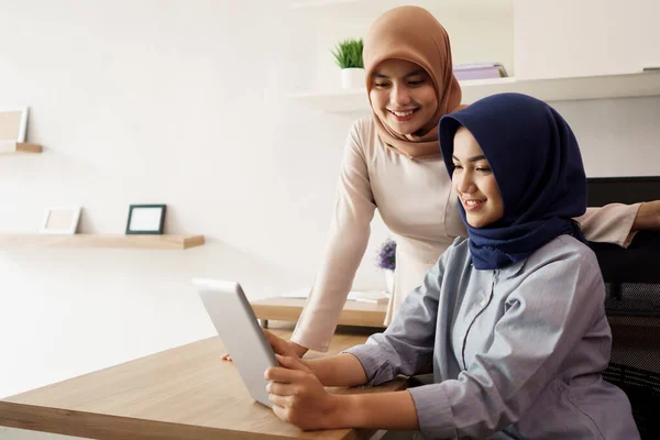 Retrato de belas mulheres muçulmanas explicando projeto em tablet para seu parceiro — Fotografia de Stock