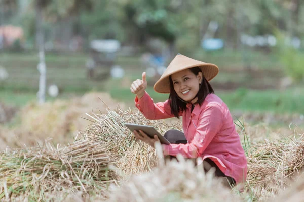 Agricultoras usan un sombrero con pulgares hacia arriba cuando están en cuclillas usando una tableta — Foto de Stock