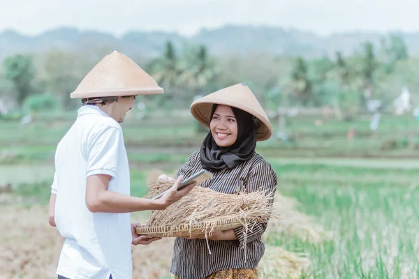 アジアの女性農家は、男性農家への竹のトレイに米の収量を示しています — ストック写真