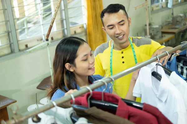 Top vista lateral casal alfaiate arrumando amostras de roupas em racks de cabide — Fotografia de Stock