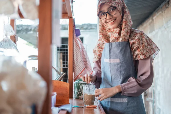 Hijab menina no avental agita o café no copo para fazer uma bebida — Fotografia de Stock