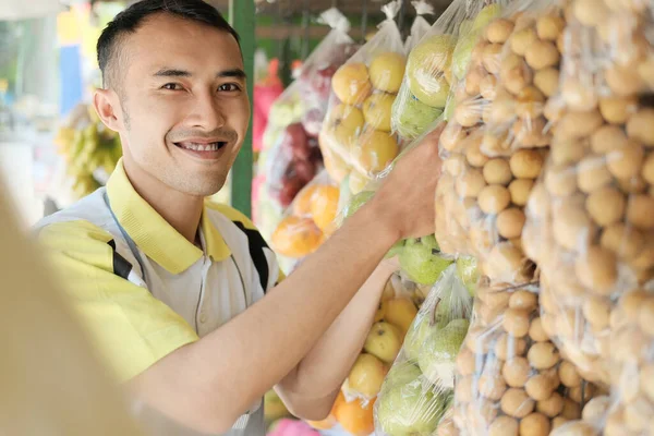 Assistente de loja organizando embalagem de frutas de plástico pendurado — Fotografia de Stock