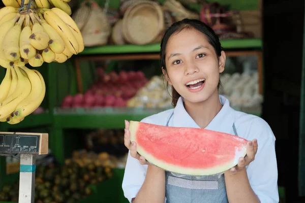 穿着围裙的漂亮女孩在水果摊里提着西瓜 — 图库照片