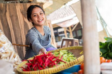 Asyalı manav kadın elinde biber dolu bir bambu tepsisiyle gülümsüyor.