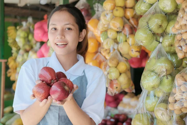 Mosolygós ázsiai hölgy bolt asszisztens szállító friss piros alma a háttérben egy friss gyümölcs — Stock Fotó