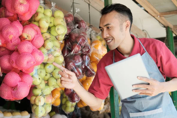 Egy férfi bolttulajdonos digitális tabletet tart, miközben ujjal mutogat a friss gyümölcsre. — Stock Fotó