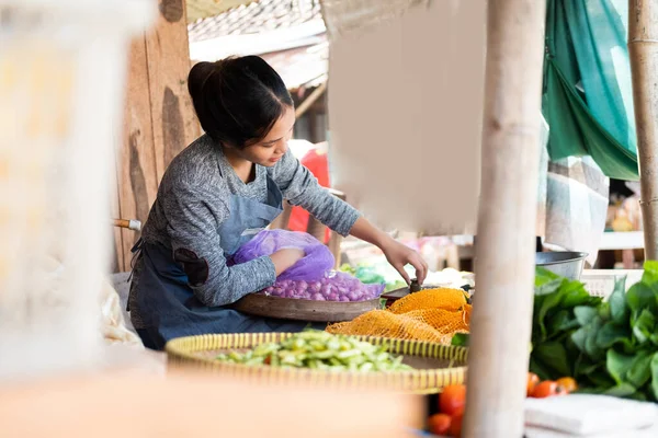Asian woman greengrocer takes onions from a sack to weigh — Stock Photo, Image