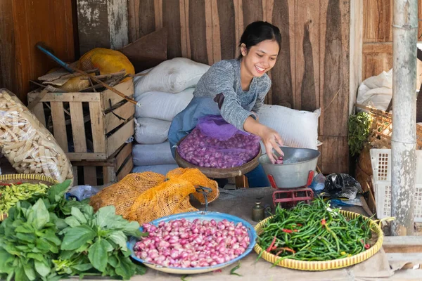 Женщина, продающая овощи, улыбается, сидя с мешком, наполненным шалотом — стоковое фото