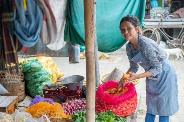 Asian woman greengrocer takes carrots out of sacks to display her vegetable stall — Stock Photo, Image