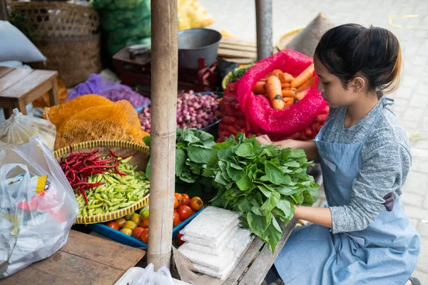 Asian woman greengrocer arranges spinach for her vegetable stall display — Stock Photo, Image