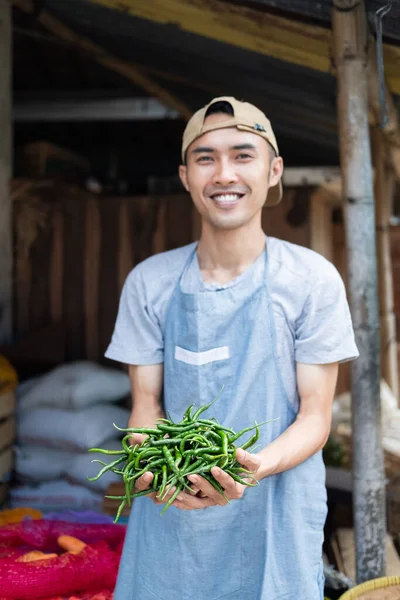 Asijské zelenina prodejce muž se usmívá, zatímco drží zelené chilli — Stock fotografie