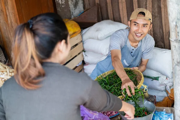 Männliche Verkäufer, die grüne Chilischoten nehmen, bedienen weibliche Käufer — Stockfoto