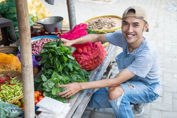 Vegetais homem de vendas de barraca sorri enquanto segurando vegetais espinafre — Fotografia de Stock