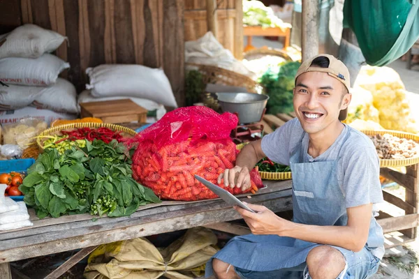 Close-up do homem que vende a barraca de legumes sorrindo ao usar o tablet pc — Fotografia de Stock