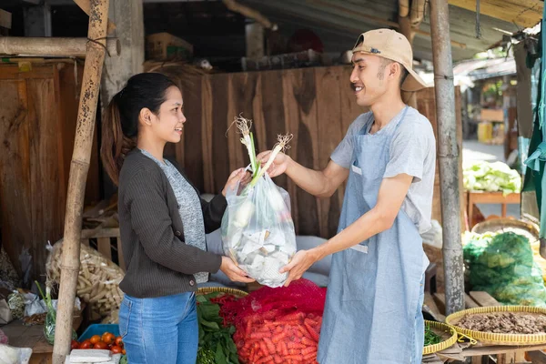 Man selling a vegetable stall gives a plastic bag of vegetables to a female buyer — Stock Photo, Image