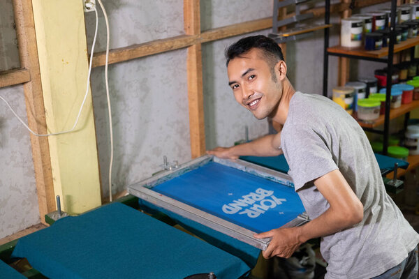male worker smiles while setting up and attaching the silkscreen frame to the hinge