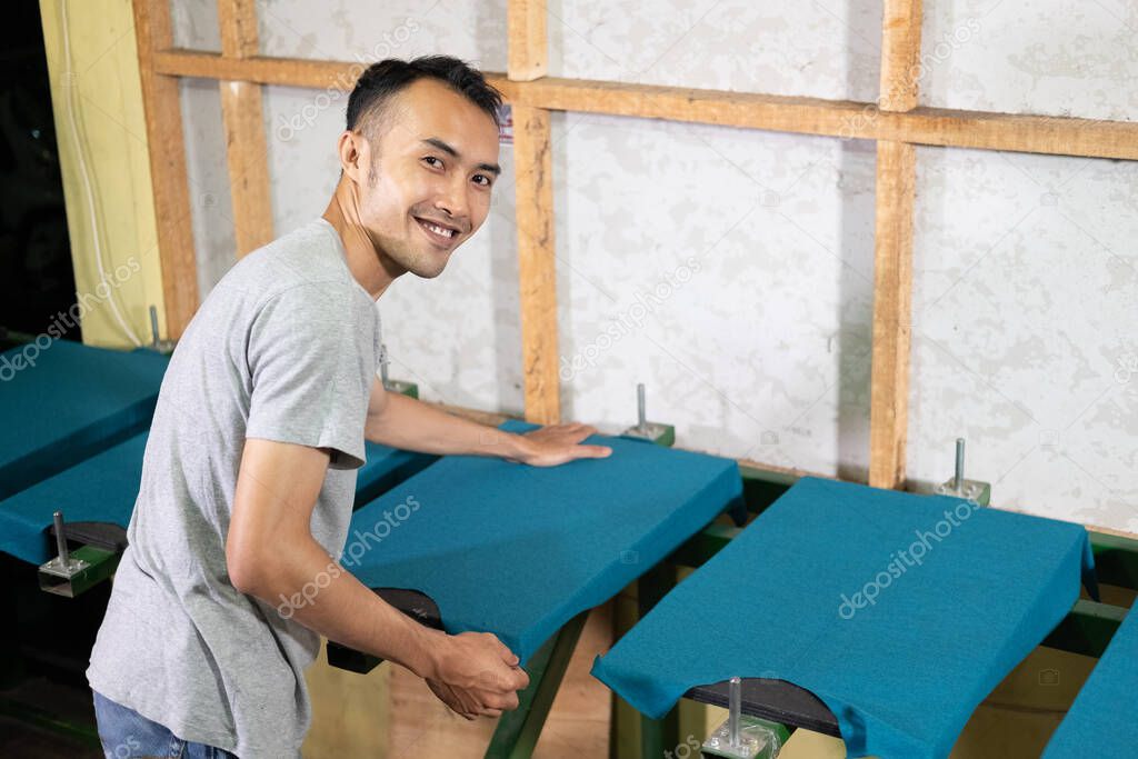 men smile while pulling the uneven part of the shirt while preparing the t-shirts