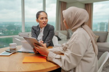 İki iş kadını, çalışmalarıyla ilgili kilit fikirleri tartışmak için modern bir ofiste işbirliği yapıyorlar.