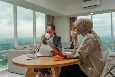 İki hırslı iş kadını, şık bir ofiste kahve eşliğinde fikir alışverişinde bulunarak işbirliğini teşvik ediyorlar.