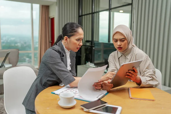 Modern bir ofiste, iki iş kadını önemli belgeler hakkında tartışıyorlar.