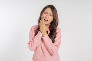 Parlak bir stüdyo ortamında, bir kadın gözle görülür şekilde diş ağrısı ve rahatsızlık belirtileri gösterir.