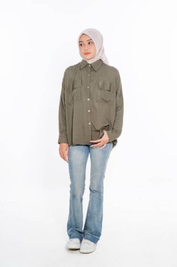 Zarif bir kadın zeytin yeşili bir gömlek giyer, kot pantolon giyer, başörtüsüyle tamamlanır.