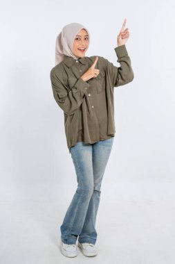 Neşeli bir kadın, sıradan giyinmiş, coşkuyla yukarıyı gösterirken, geniş bir gülümseme içinde.