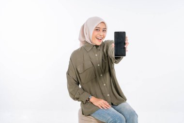 Genç bir kadın, paylaşmak için canlı bir selfie çekerken akıllı telefonuyla neşe içinde poz veriyor.