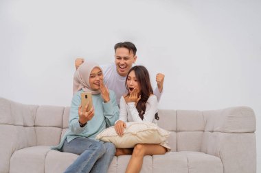 Üç arkadaş coşkulu bir selfie için toplanıyor, heyecan ve saf mutluluk sergiliyorlar.