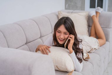 Mutlu genç bir kadın, koltuğunda rahat bir şekilde uzanırken telefonuyla sohbet ediyor.